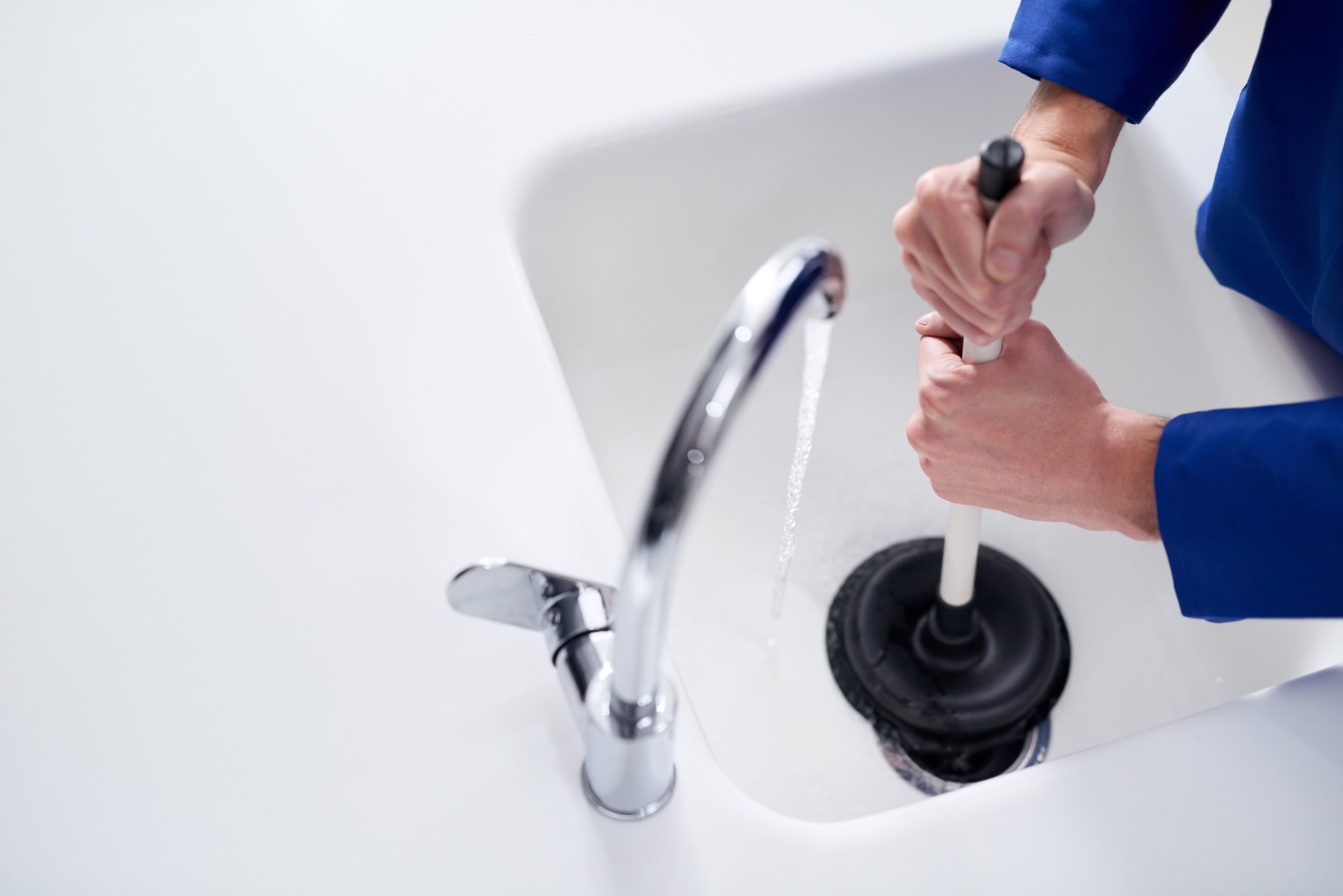 A person using a plunger in a white sink to clear a blockage.
