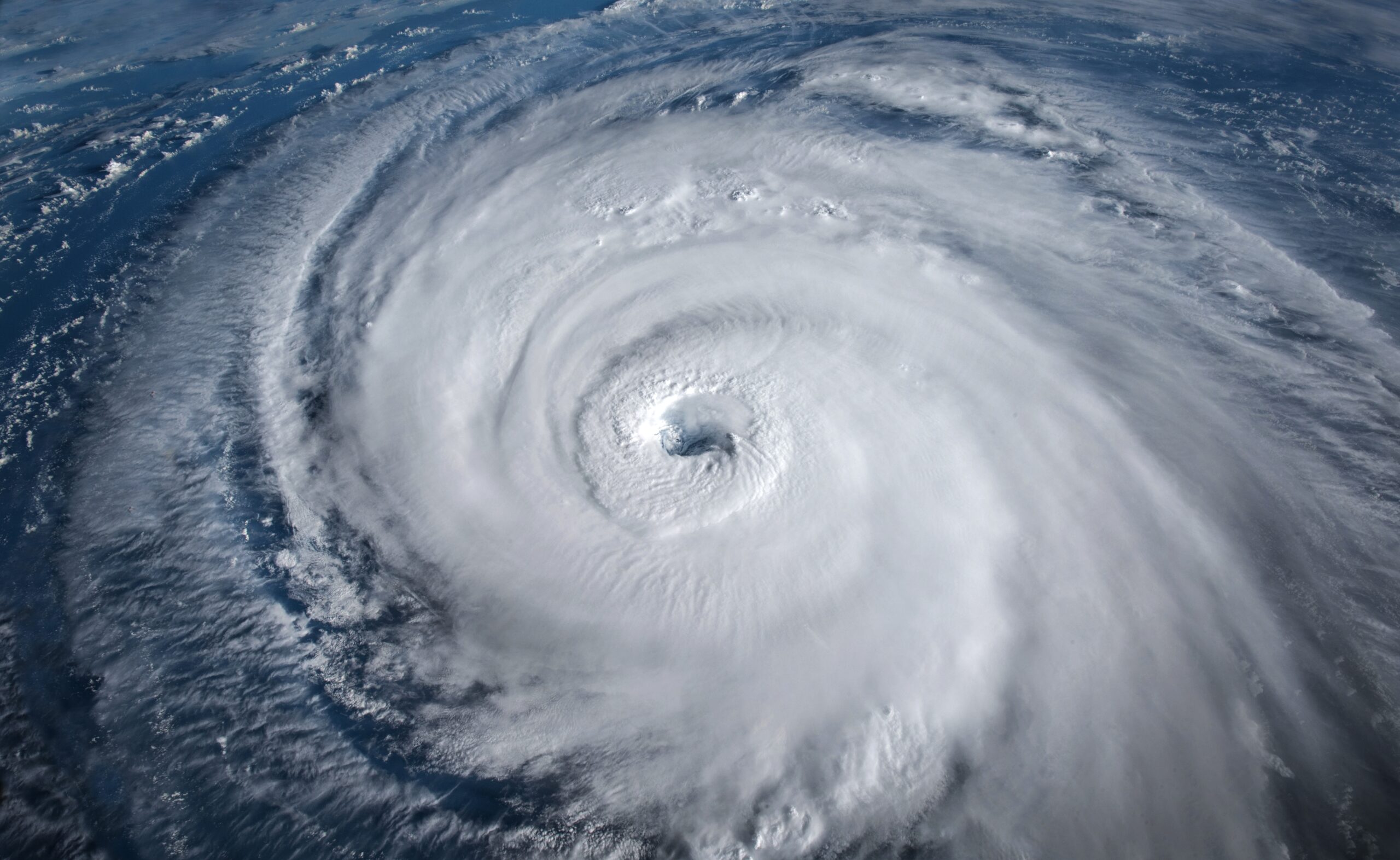 Aerial view of a massive hurricane with a well-defined eye, swirling clouds, and extending spiral arms over the ocean.